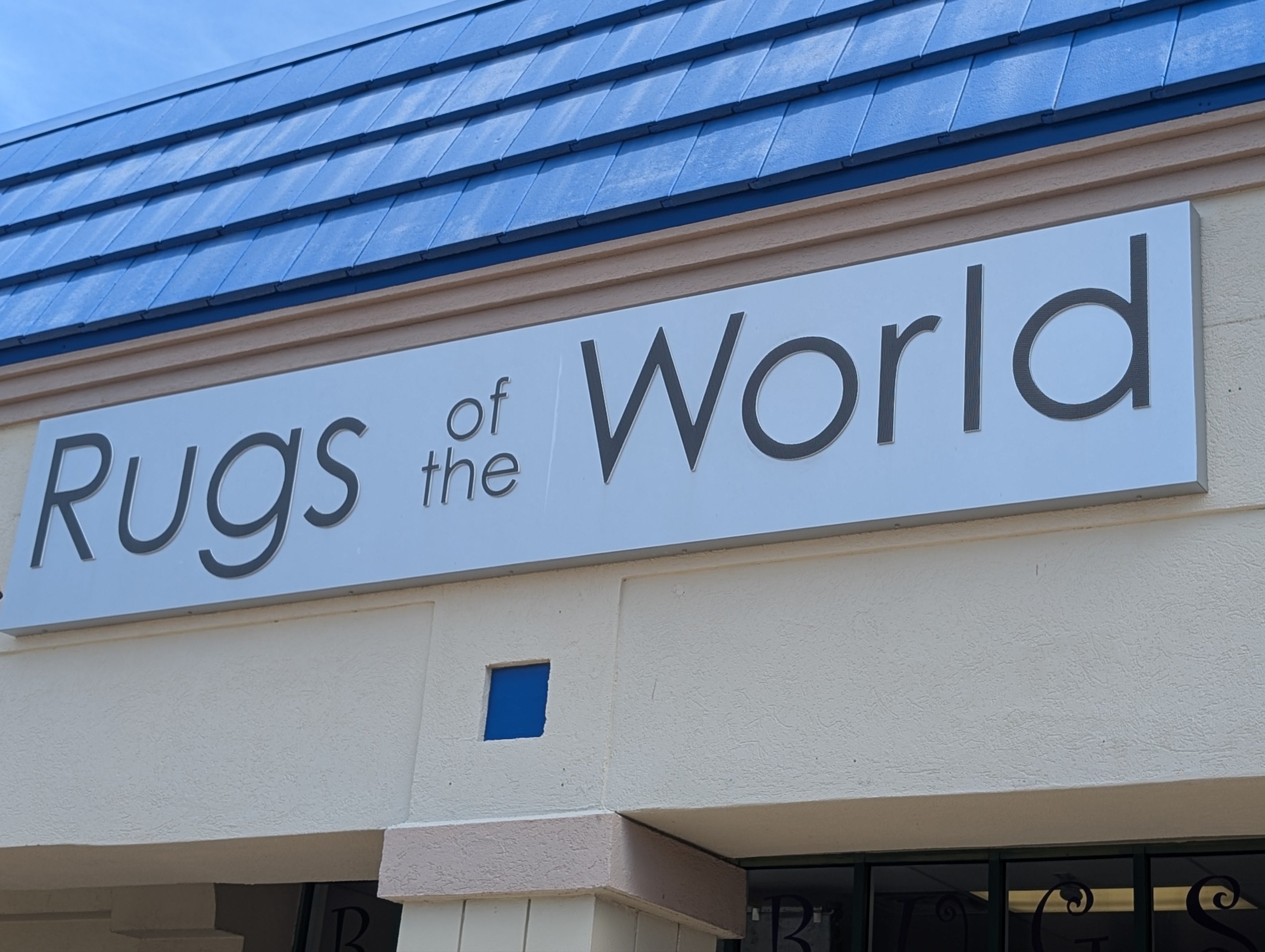 Store sign for 'Rugs of the World' on a building facade.